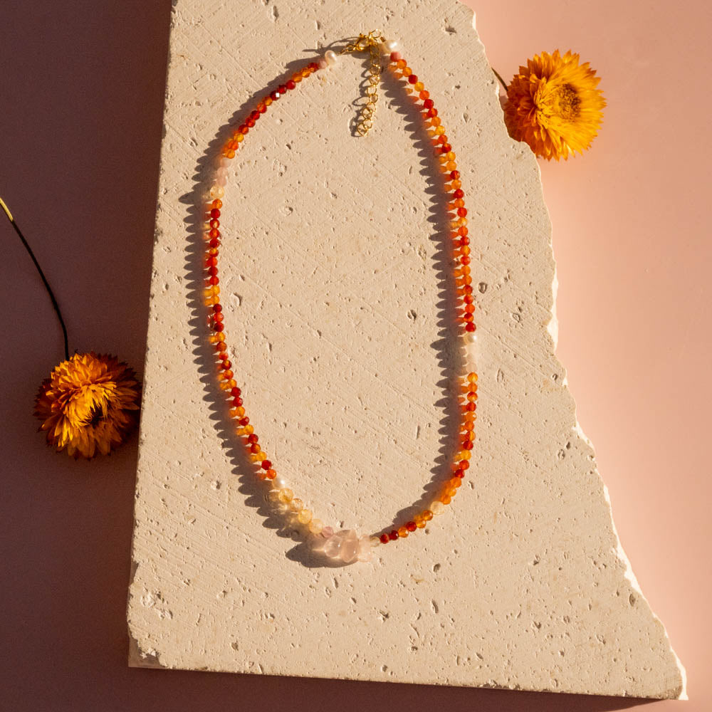 Sun chaser Necklace with carnelian beads on a textured surface with flowers