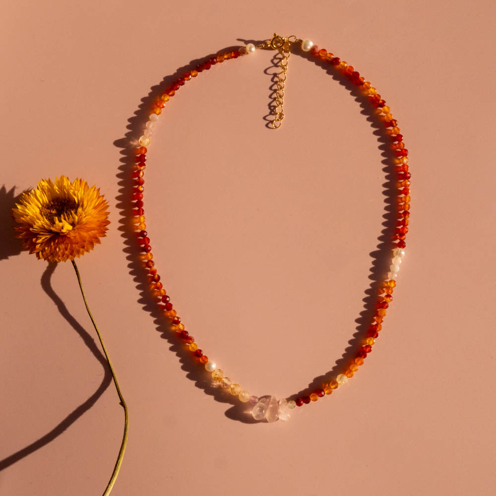 Necklace with orange and red beads and a yellow flower on a pink background