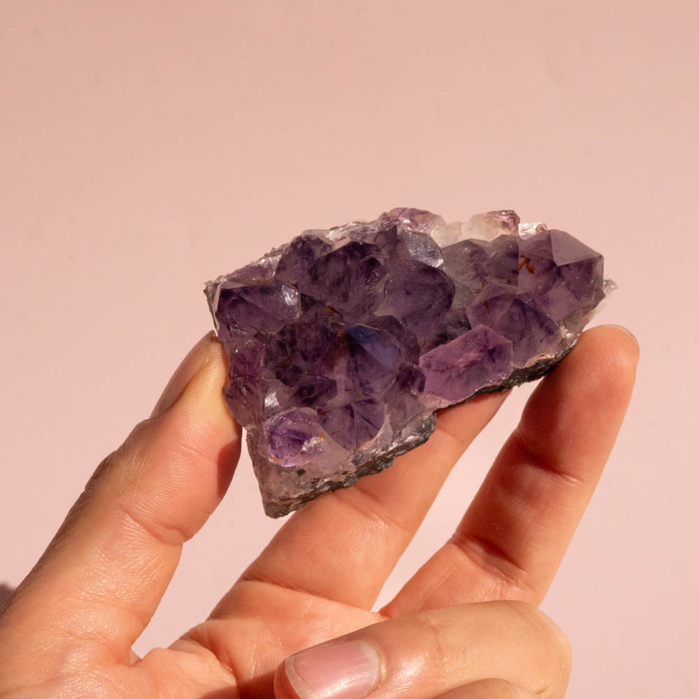 Hand holding a purple crystal against a pink background
