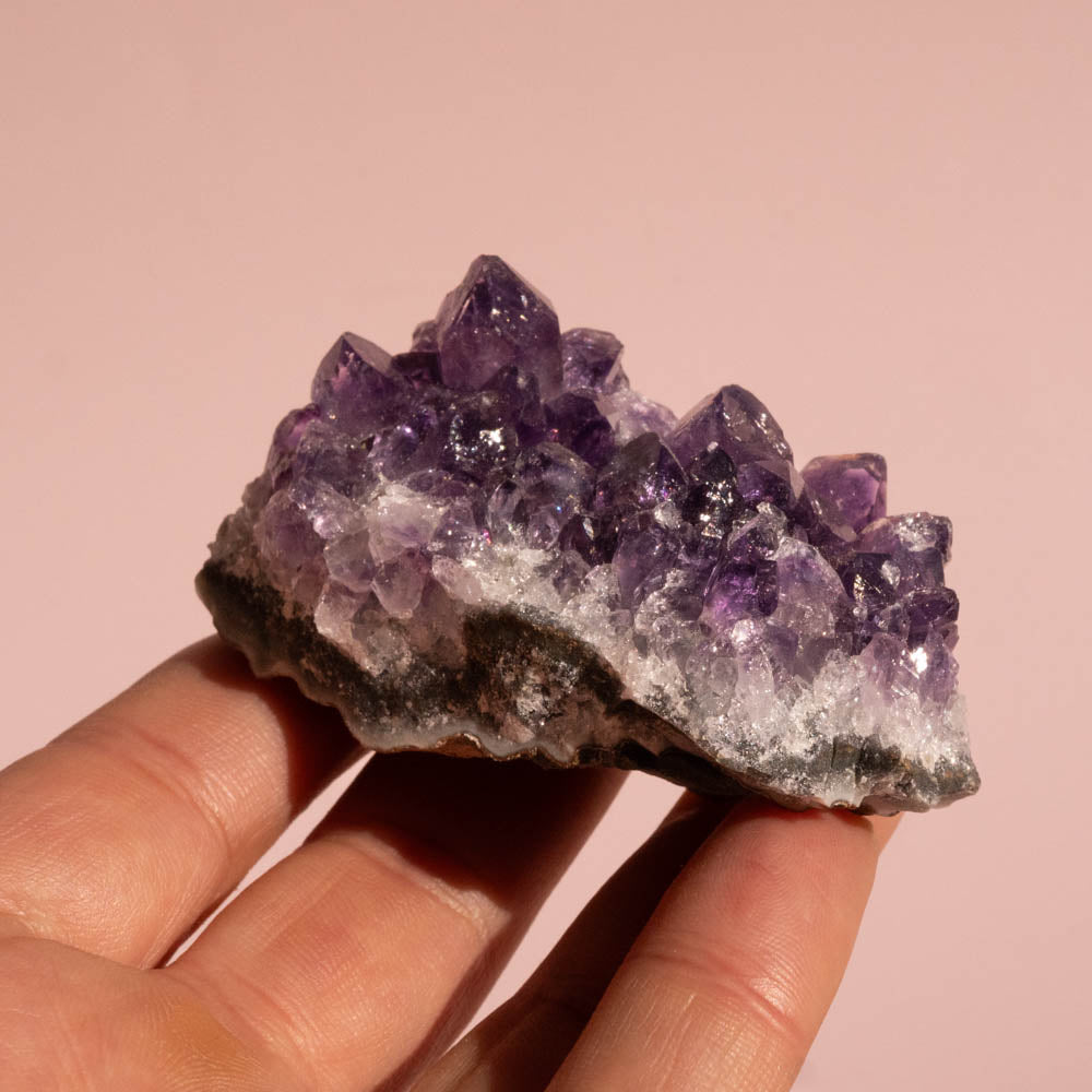 Amethyst crystal cluster held in a hand against a pink background