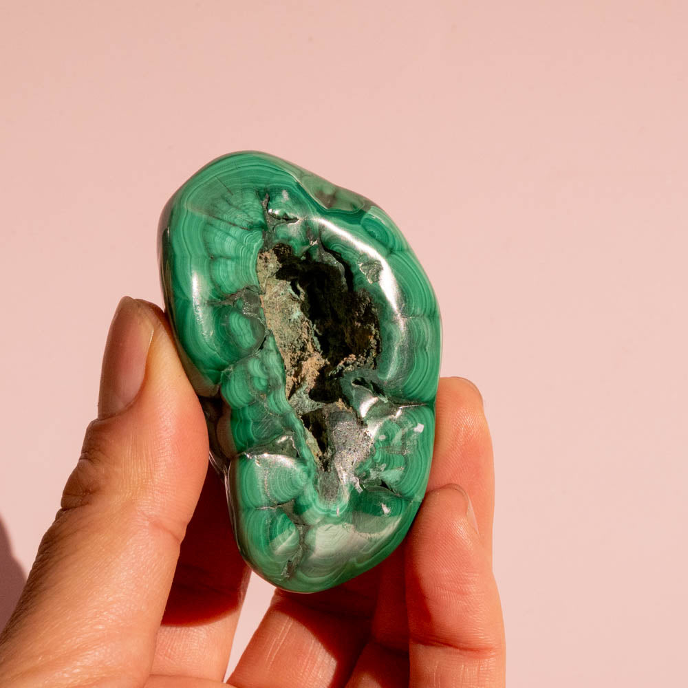Hand holding a green malachite stone against a pink background