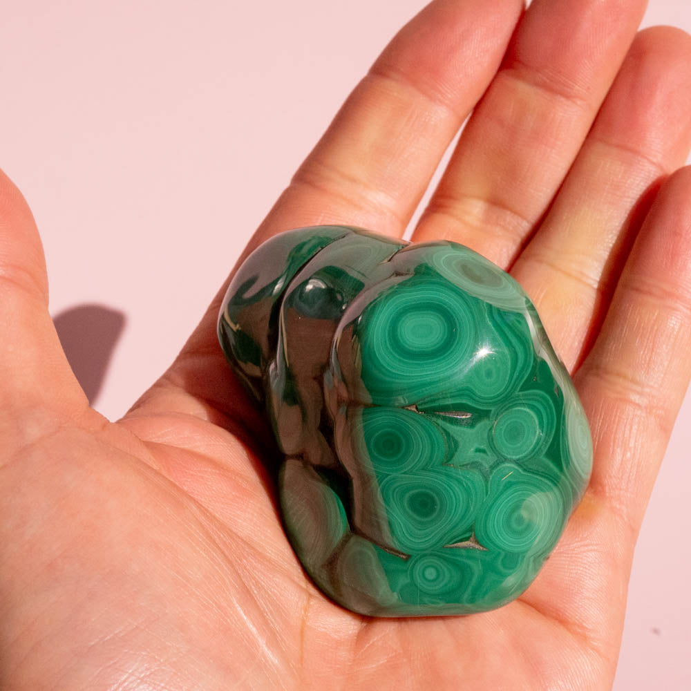 Hand holding a green malachite stone against a pink background