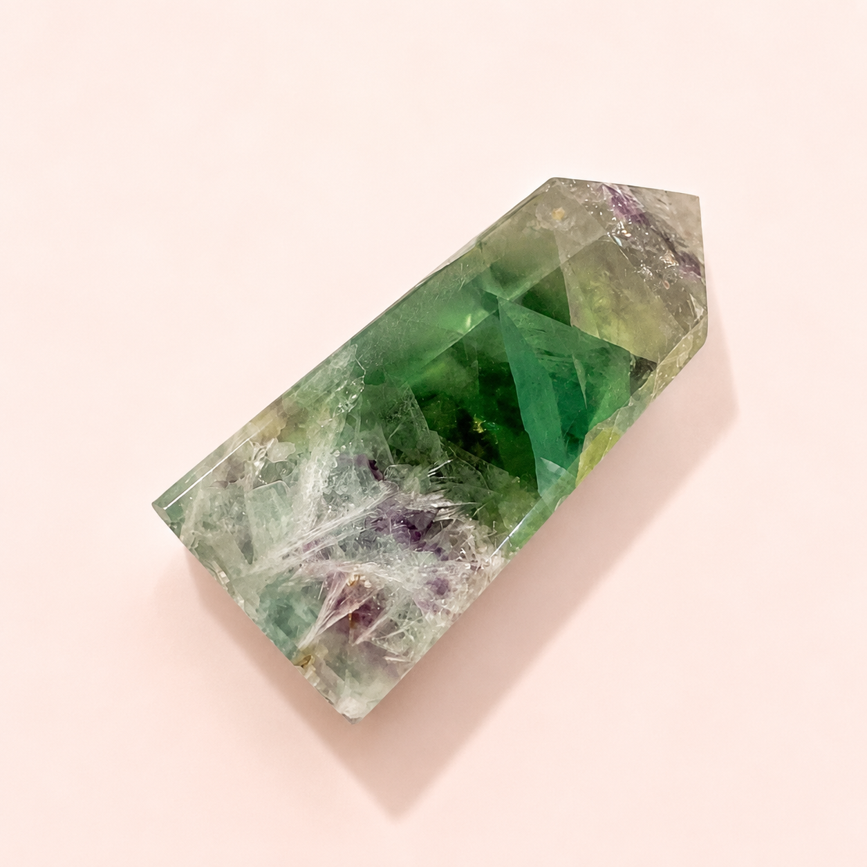 Rainbow Fluorite with natural inclusions and purpleish veining, photographed on a soft pale pink background.