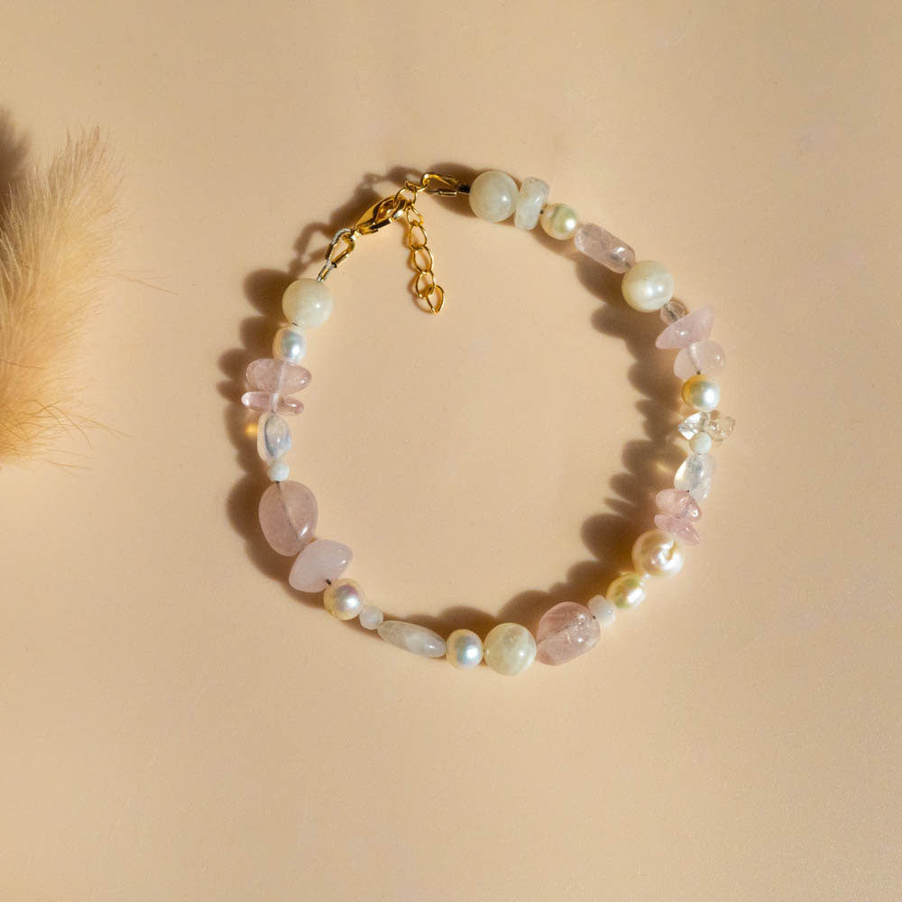 Beaded bracelet with rose quartz crystals and fresh water pearls and gold chain on a beige background