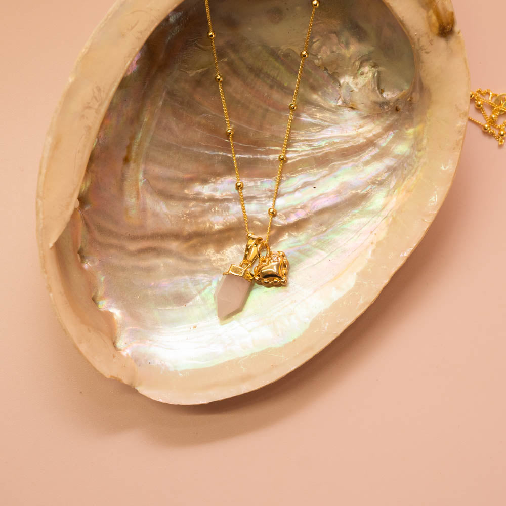 Rose quartz point crystal pendant and heart charm on gold ball chain
in abalone shell