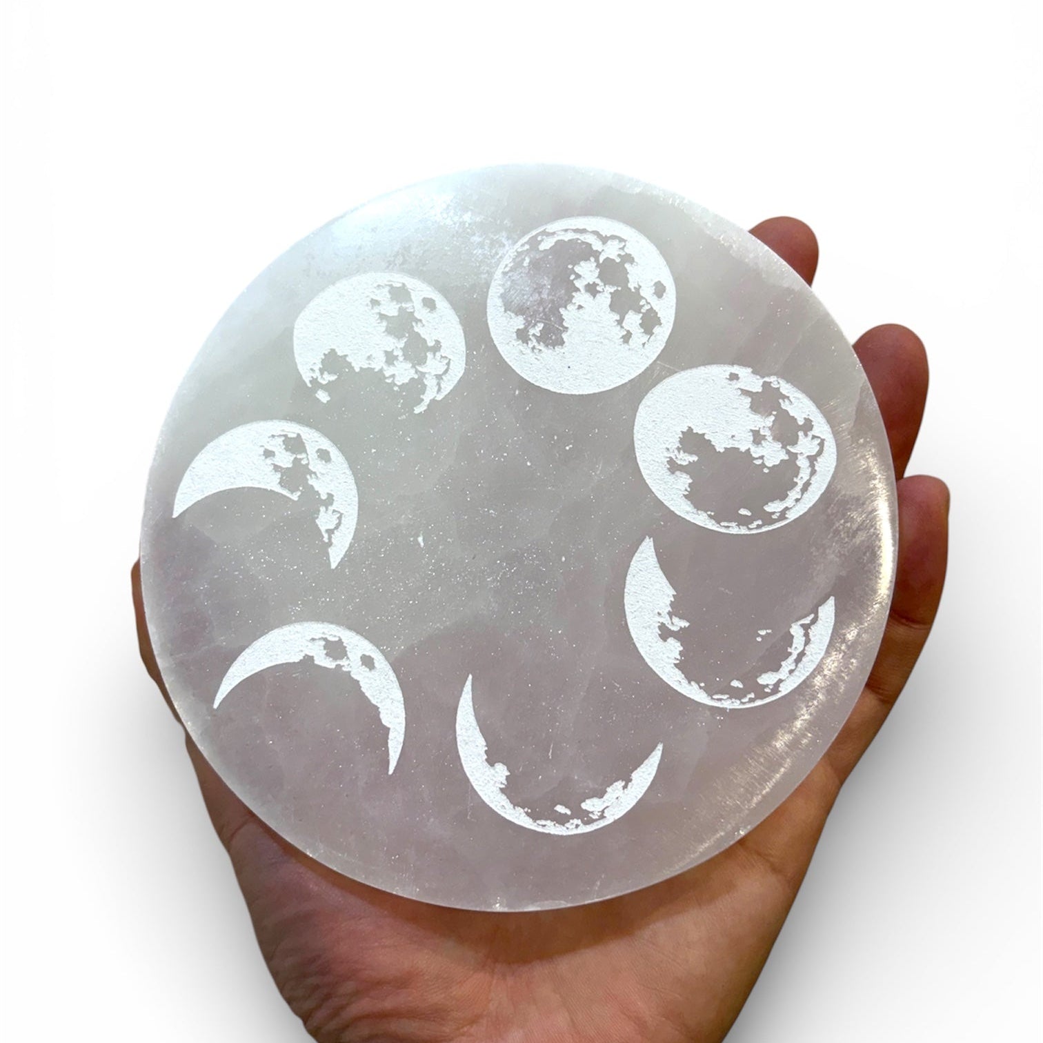 Hand holding a selenite crystal with moon phase etchings on a white background