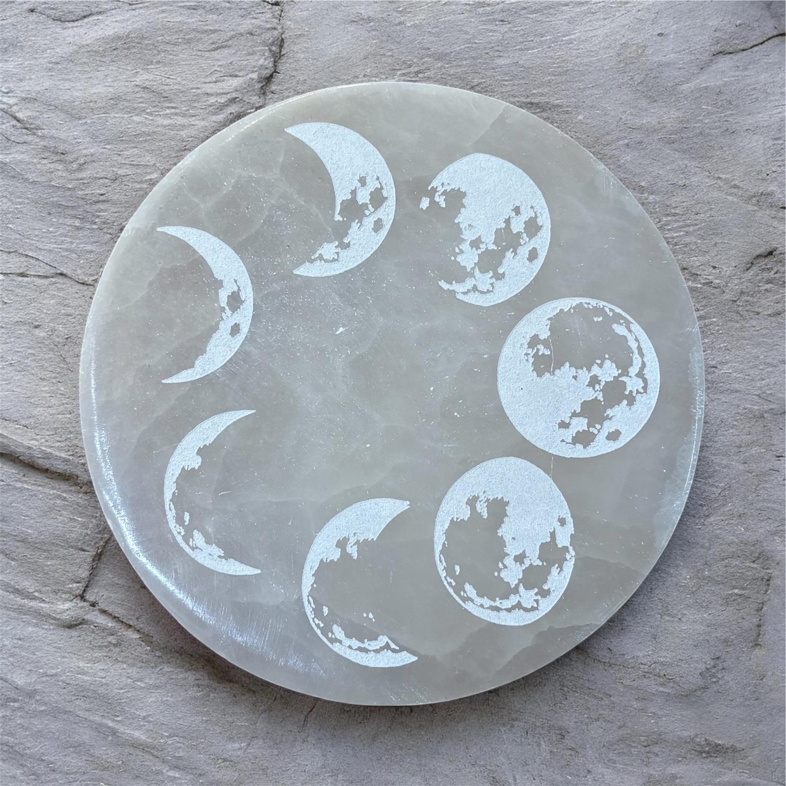 Round selenite charging plate with moon phase carvings on a wooden surface