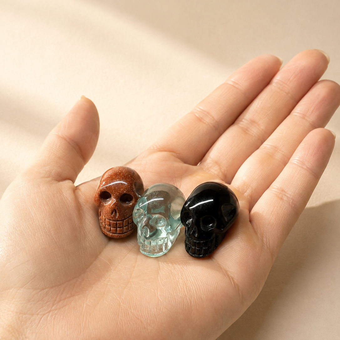 Three small carved skull-shaped, resting on an open hand against a warm beige background.