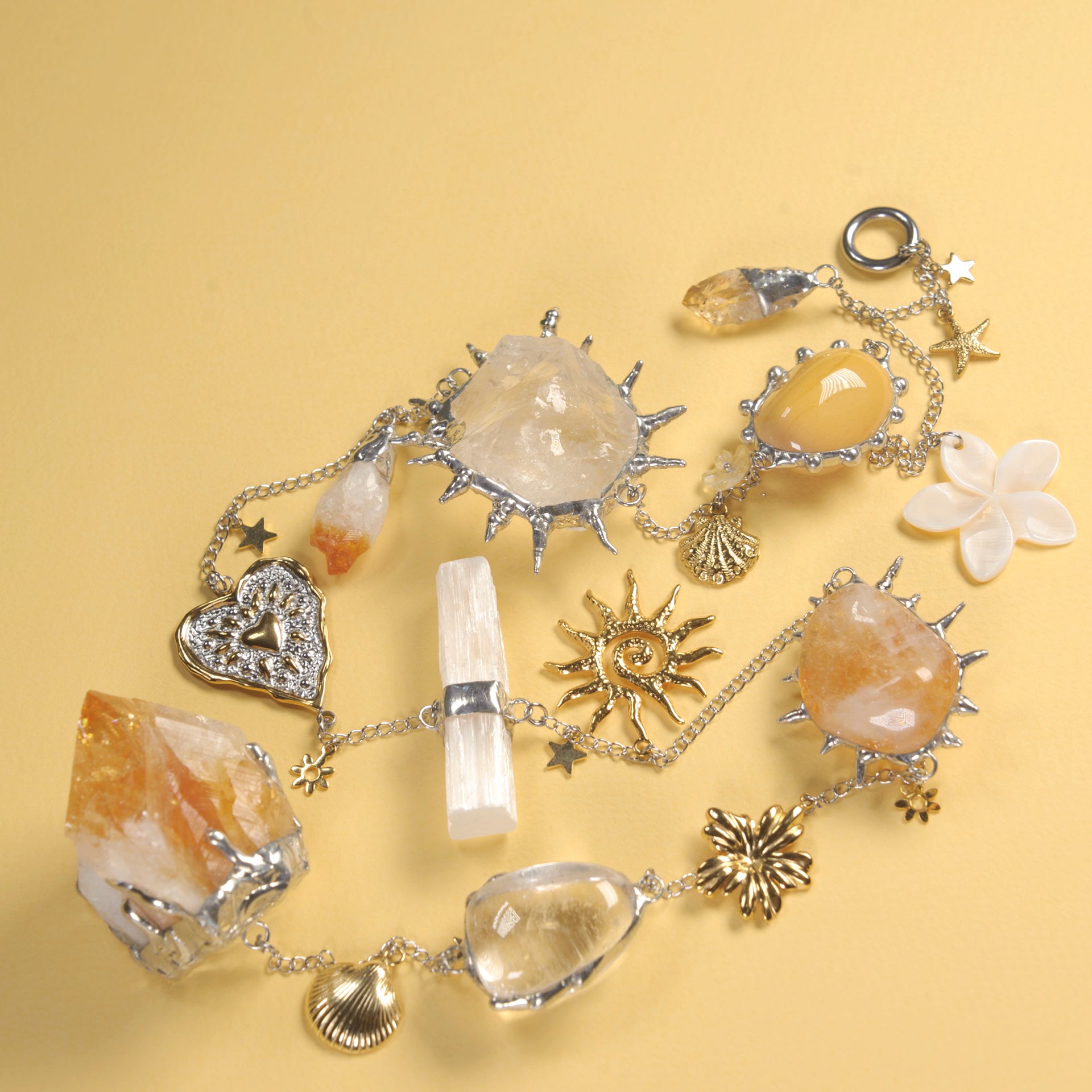 A silver chain bracelet decorated with various crystals, gemstones, and celestial charms, displayed on a solid pale yellow background.