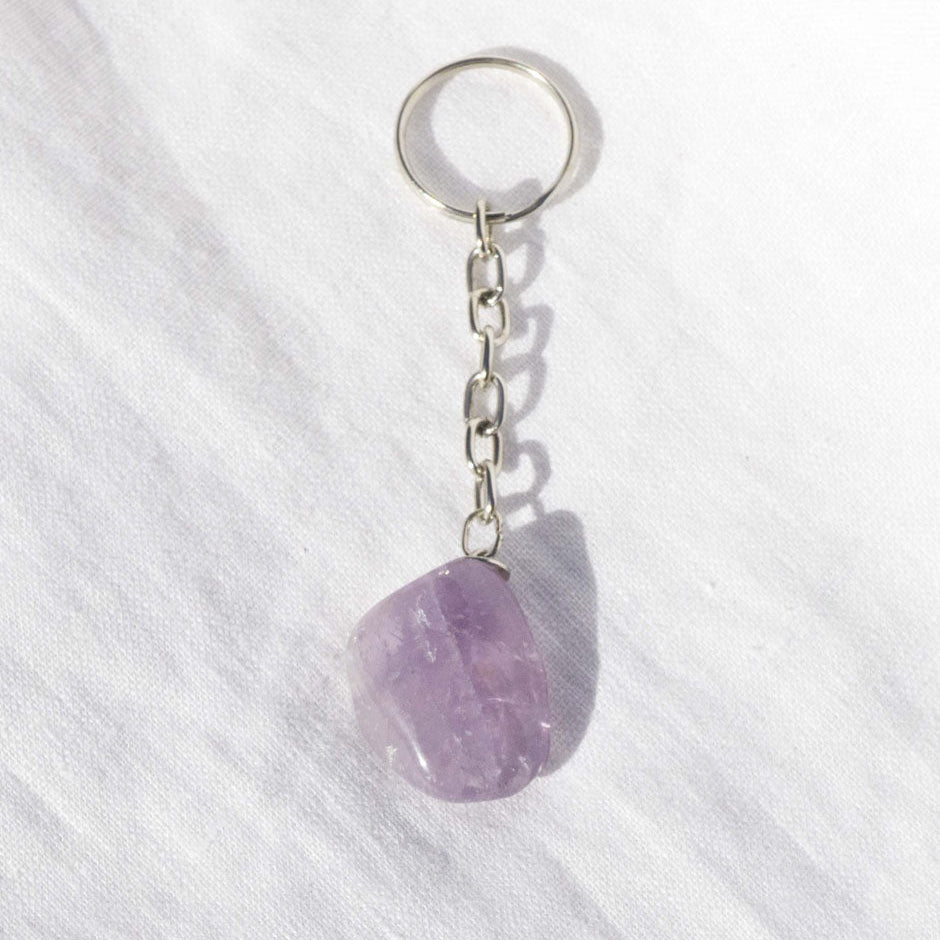 A smooth, purple amethyst gemstone attached to a silver keyring, displayed on a white textured surface.